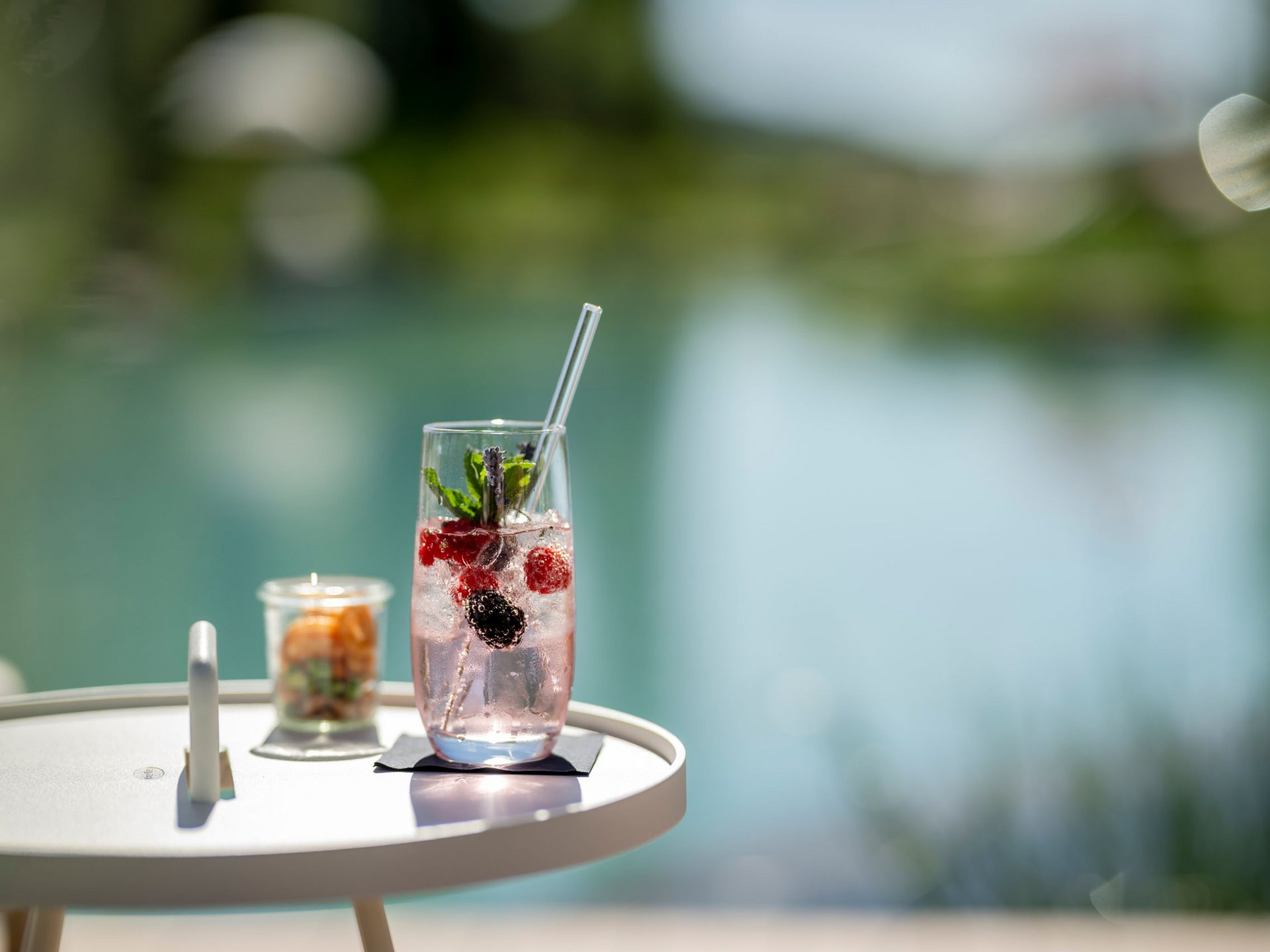 Erfrischendes Getränk mit Beeren und Minze auf einem weißen Tisch am Wasser
