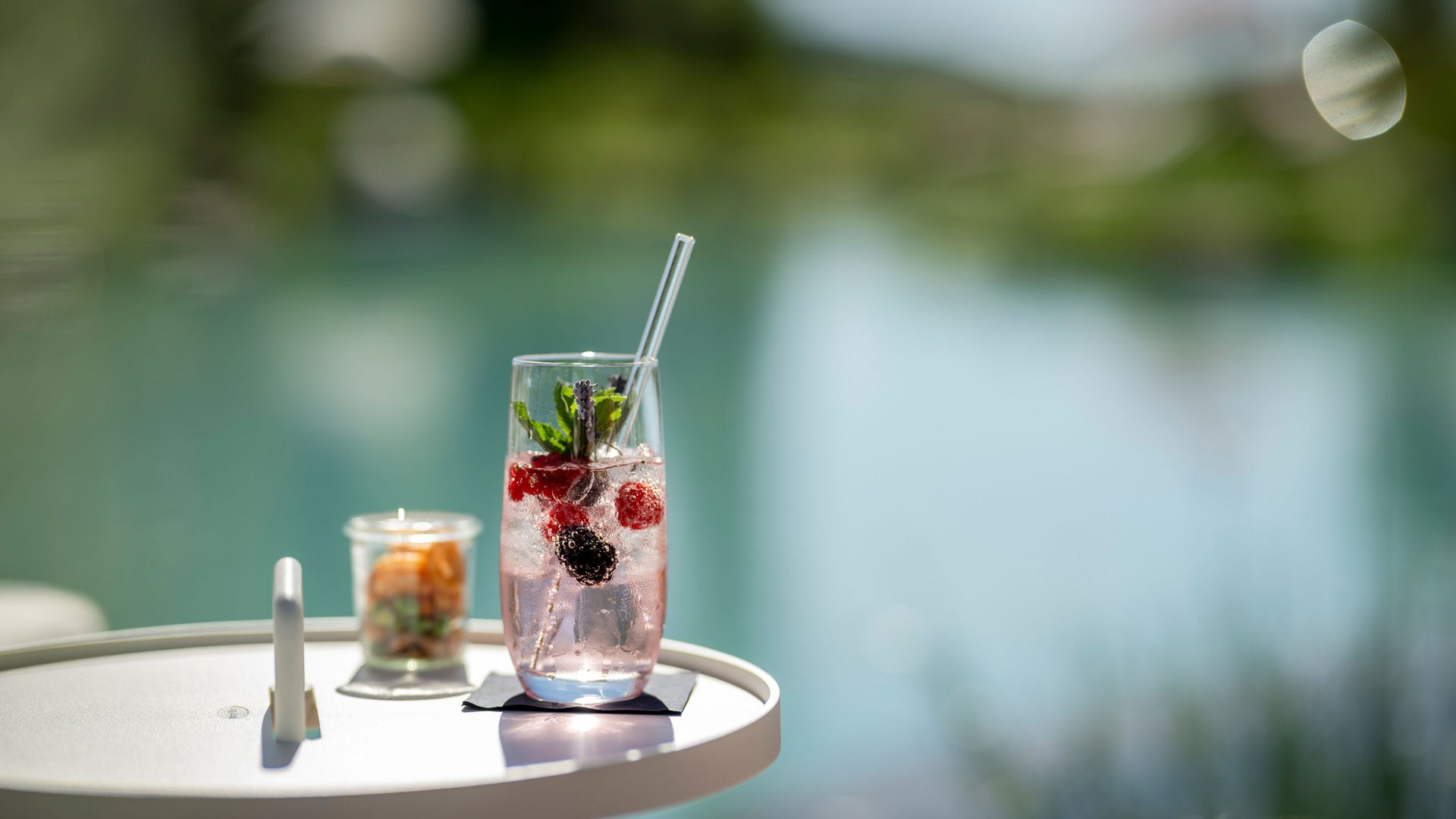 Refreshing berry and mint drink on white table by the water