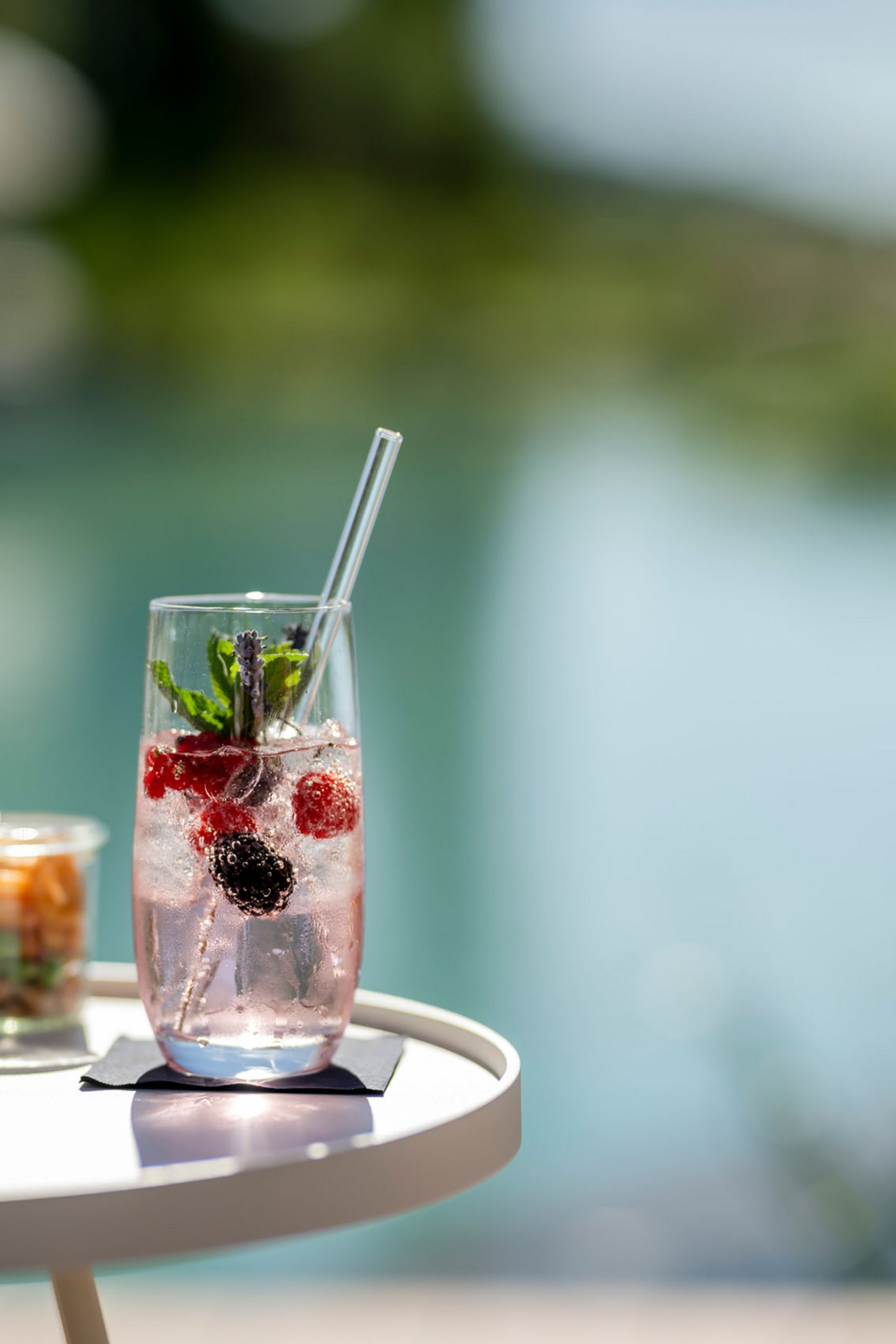 Erfrischendes Getränk mit Beeren und Minze auf einem weißen Tisch am Wasser