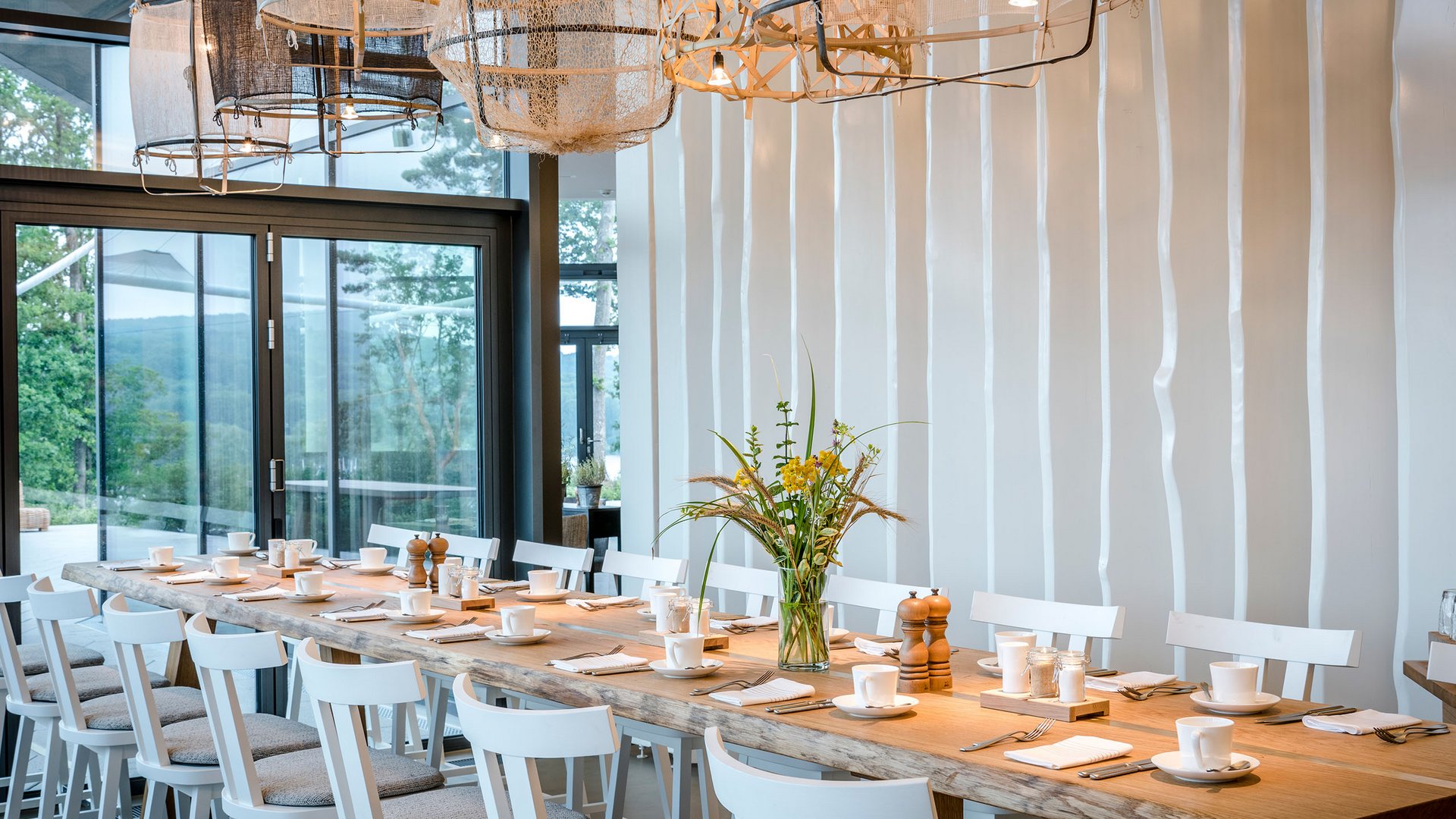 Large dining table with white chairs and modern lights in a bright room