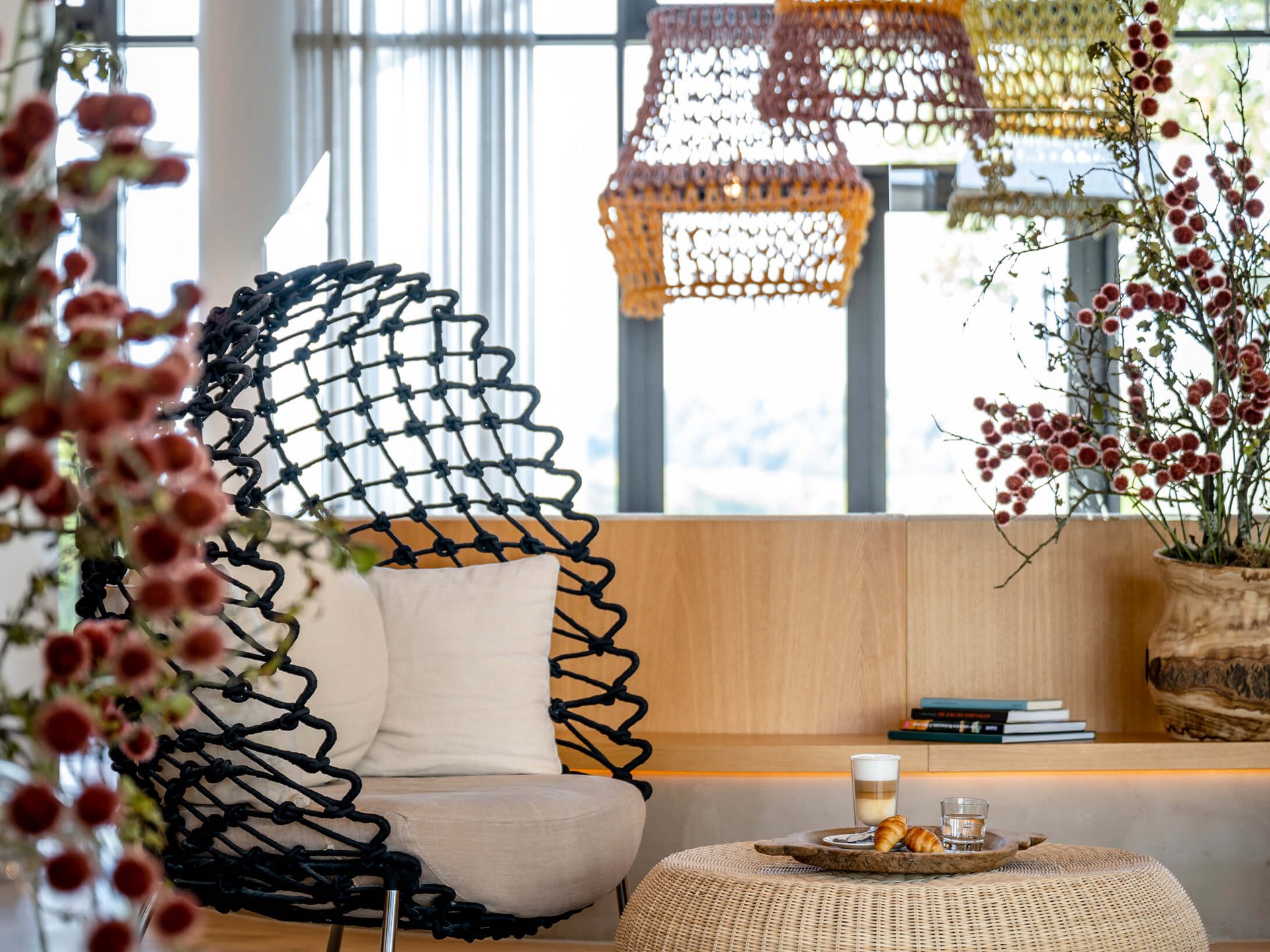 Moderner Wohnbereich mit Korbsessel, Hocker und Dekorationen bei Tageslicht