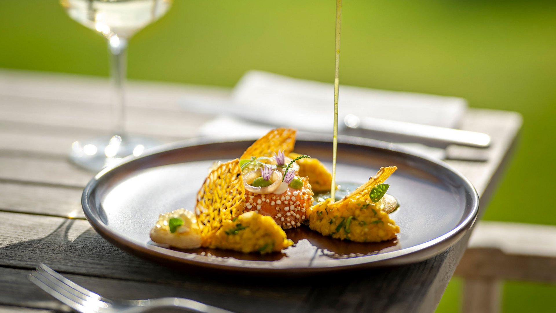 Hand pouring green sauce over an artfully plated gourmet dish outdoors