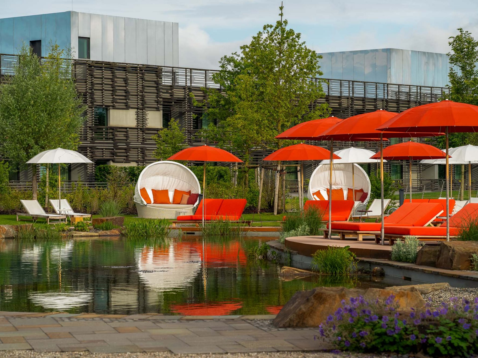 Outdoor-Liegestühle und Schirme in Rot und Weiß neben einem Teich im Gartenbereich