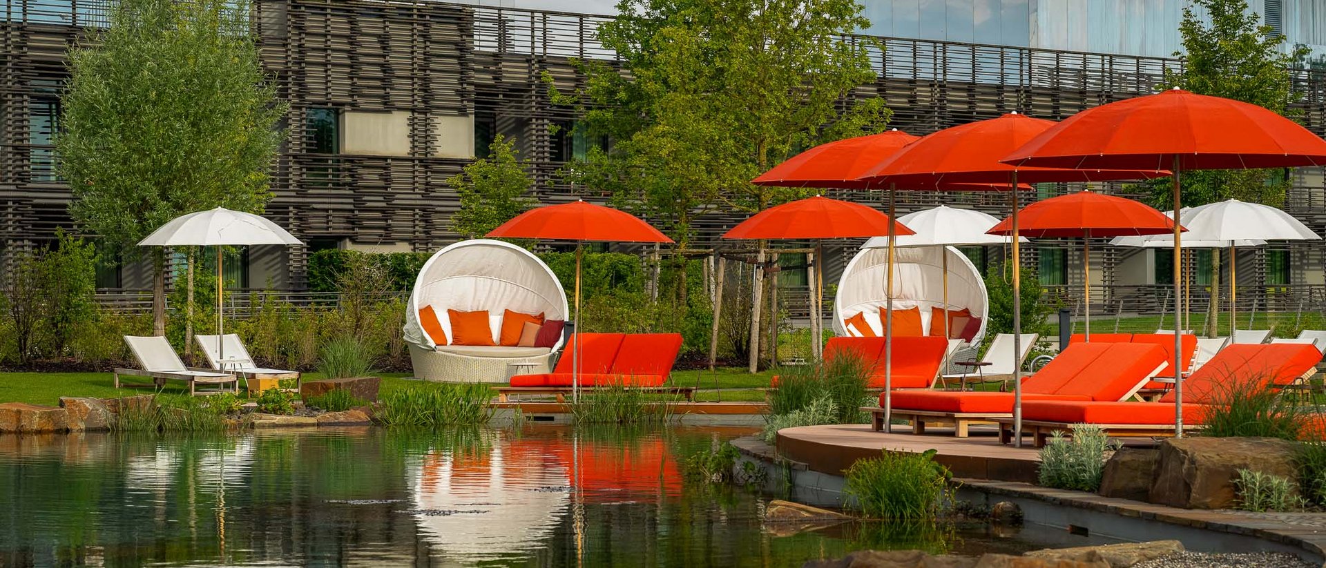 Outdoor-Liegestühle und Schirme in Rot und Weiß neben einem Teich im Gartenbereich