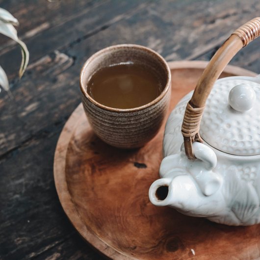 Weißer Teekessel und Tasse mit Tee auf Holztablett