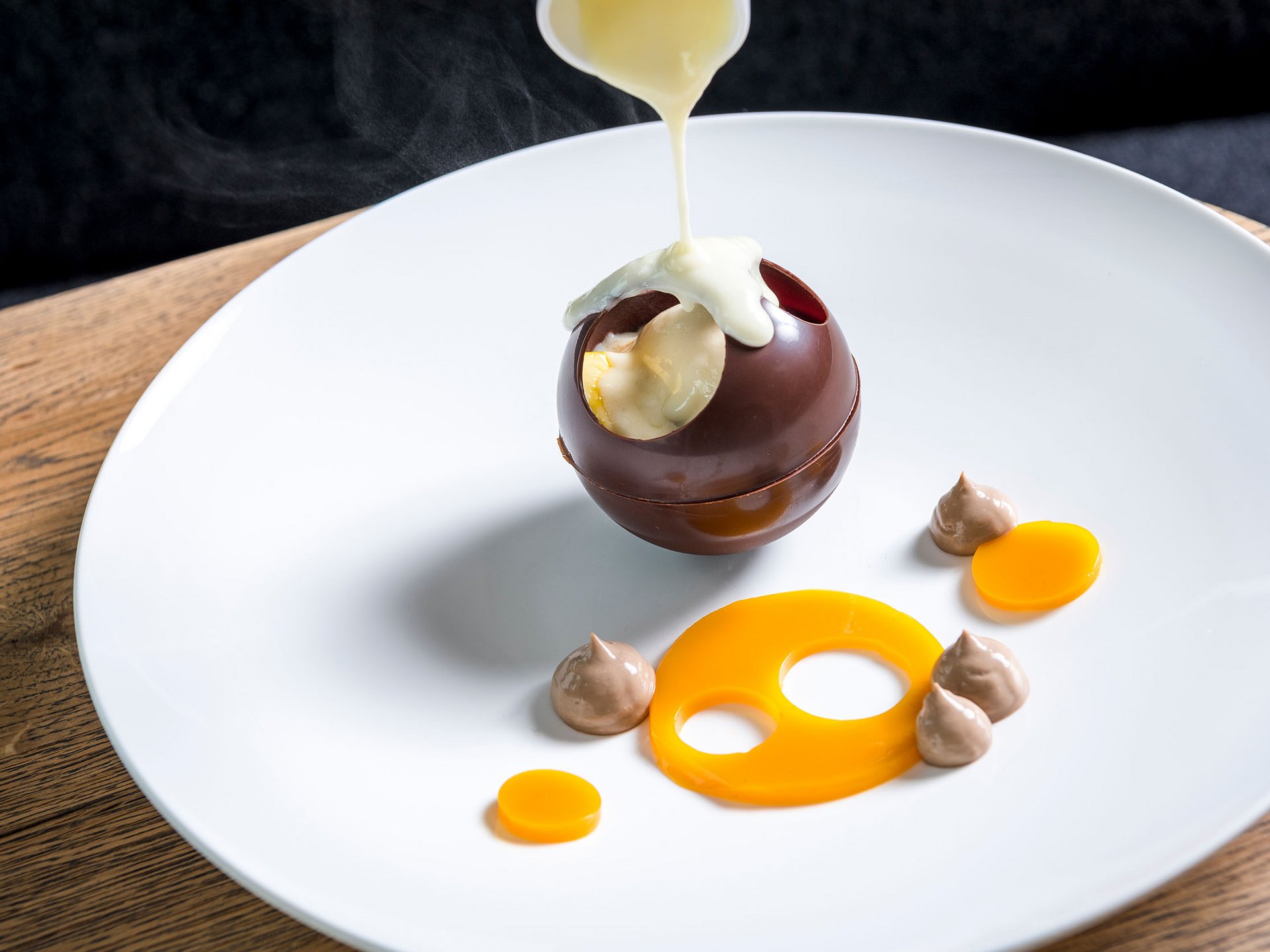 Sauce chaude versée sur une sphère en chocolat creuse sur une assiette blanche
