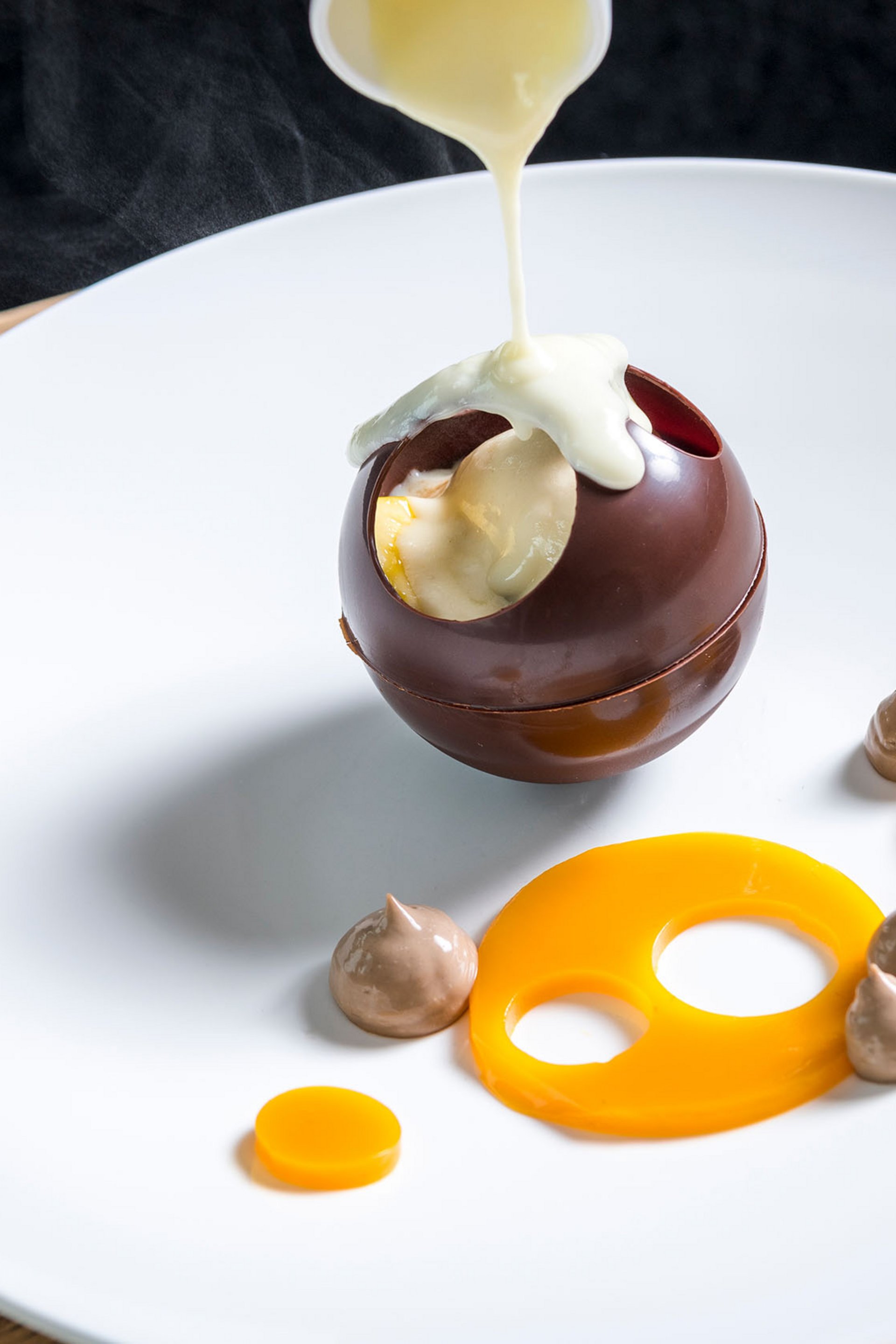 Hot sauce poured over hollow chocolate sphere on white plate