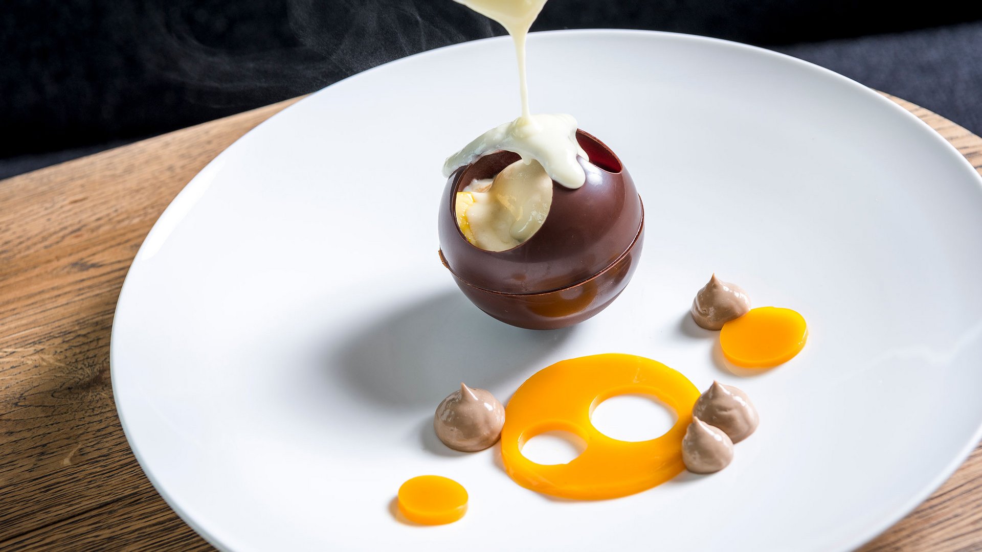 Hot sauce poured over hollow chocolate sphere on white plate