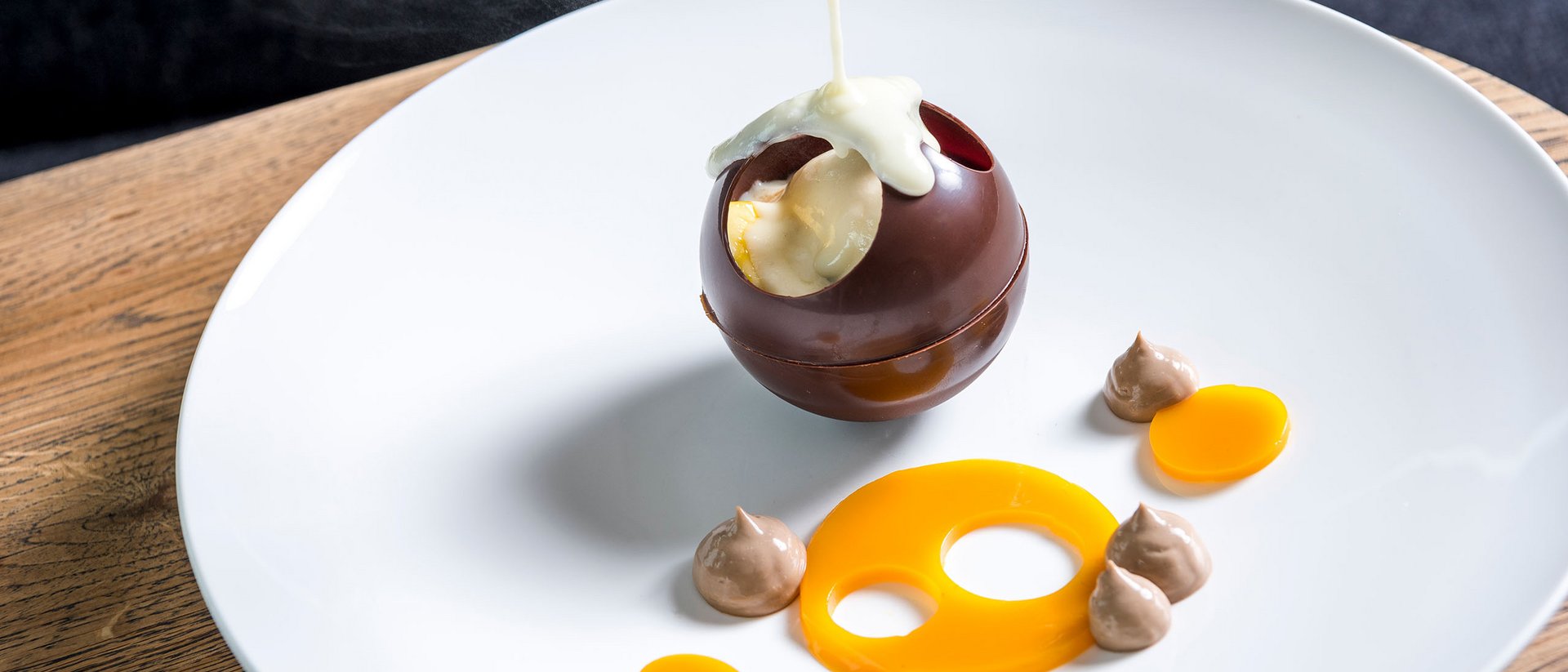 Sauce chaude versée sur une sphère en chocolat creuse sur une assiette blanche