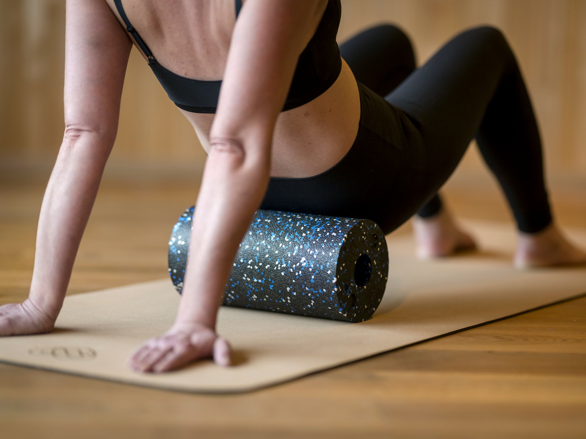 Frau nutzt Schaumstoffrolle zur Muskelmassage auf Yoga-Matte