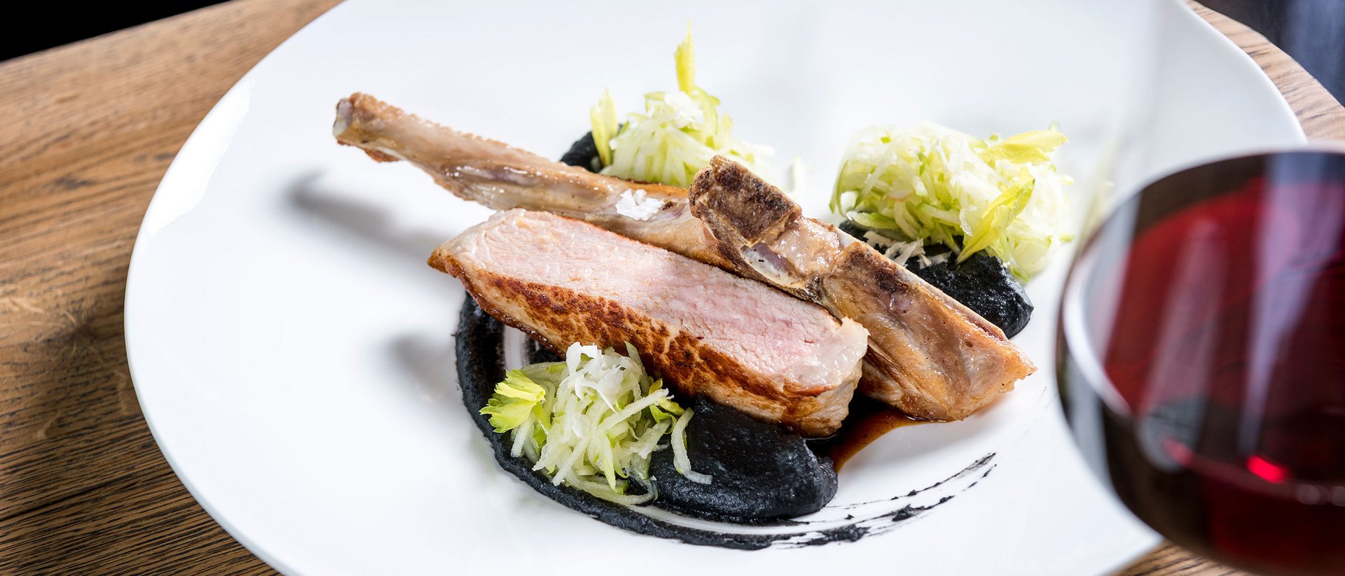 Côtelette d'agneau rôtie avec sauce noire, salade et verre de vin rouge