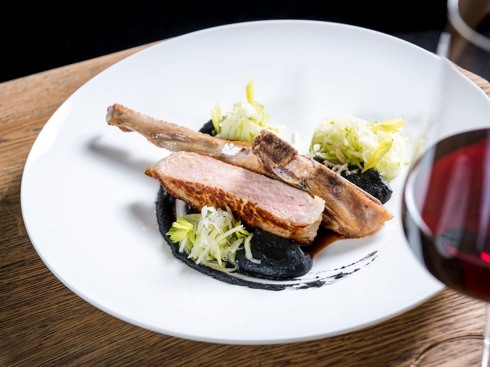 Gebratenes Lammkotelett mit schwarzer Sauce, Salat und Rotwein im Glas