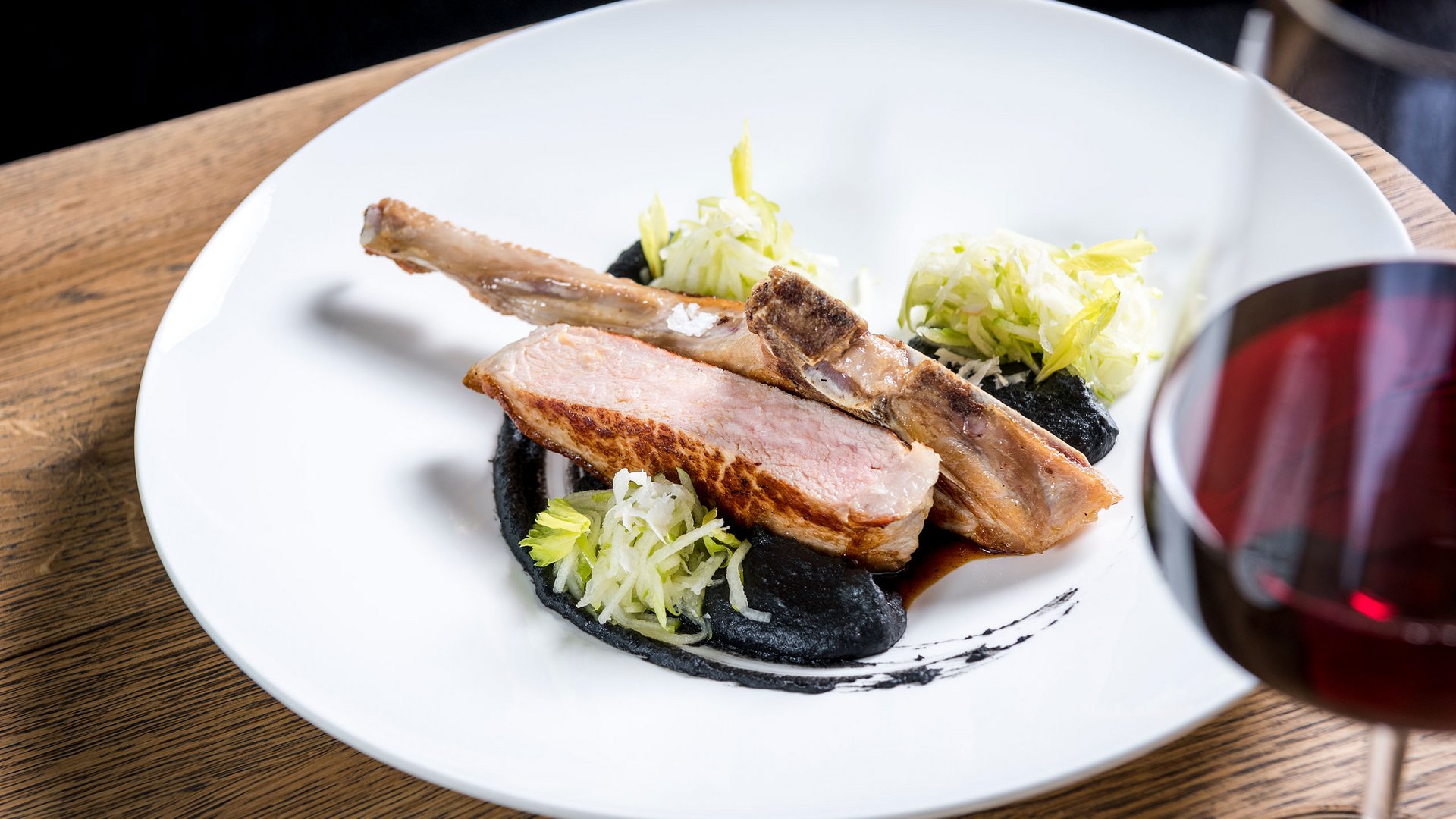 Côtelette d'agneau rôtie avec sauce noire, salade et verre de vin rouge