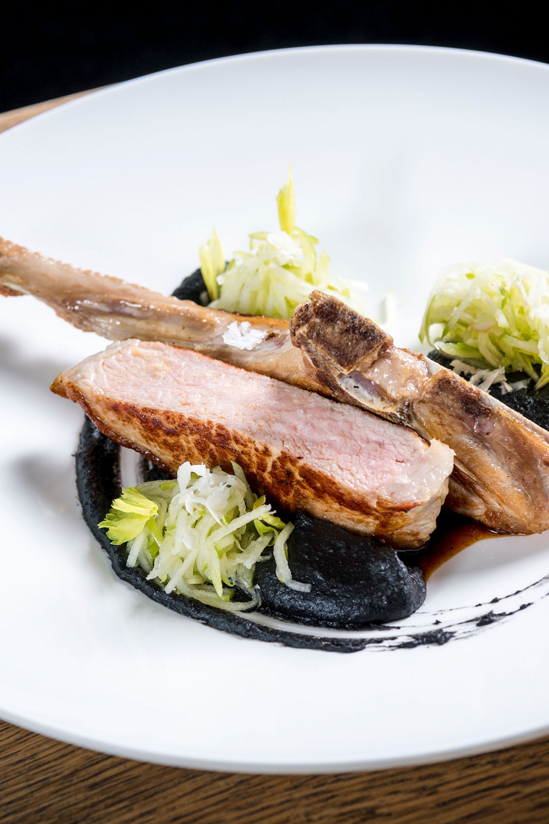 Côtelette d'agneau rôtie avec sauce noire, salade et verre de vin rouge