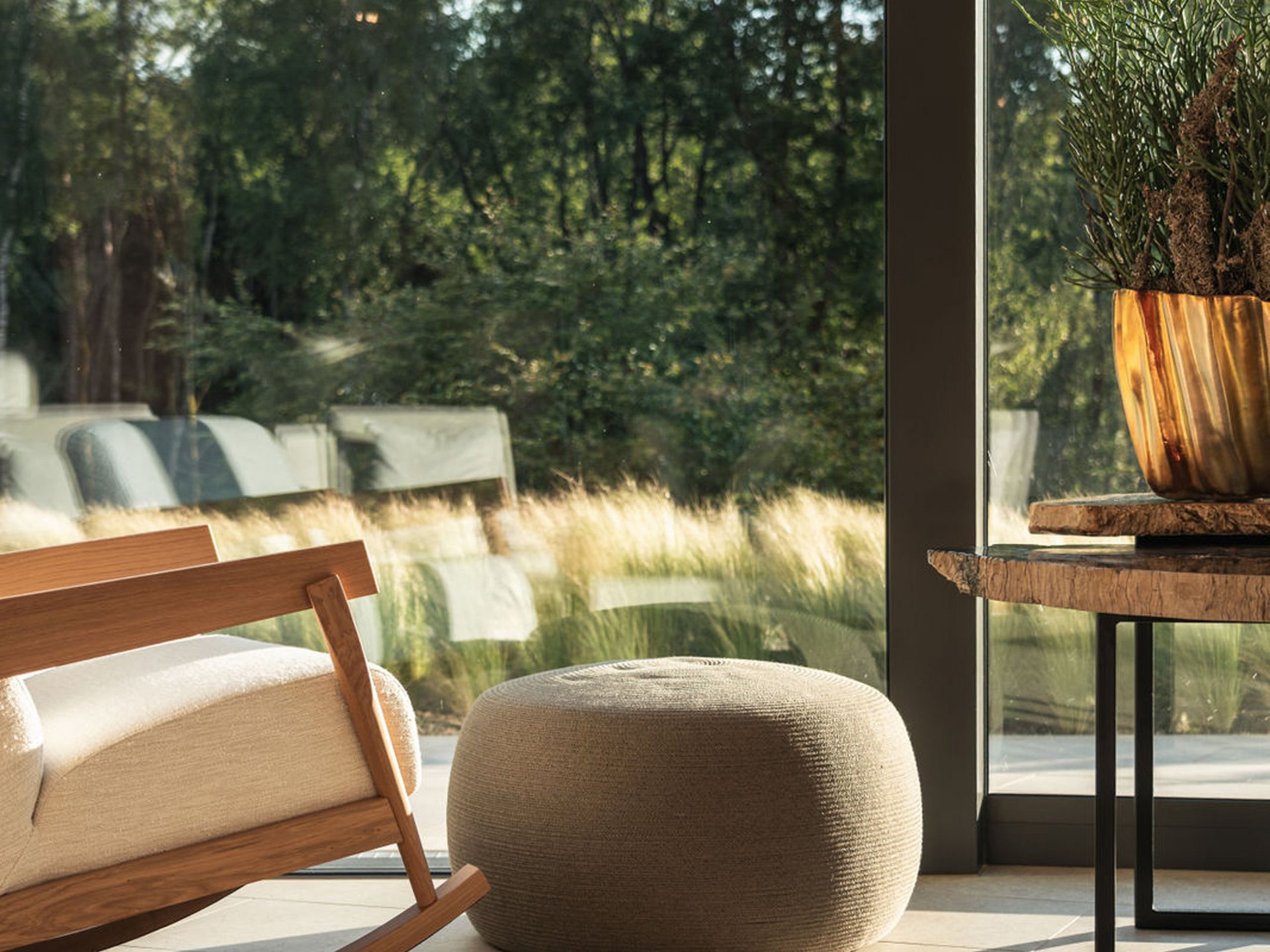 Cozy rocking chair, pouf, and table by large window overlooking green outdoor area