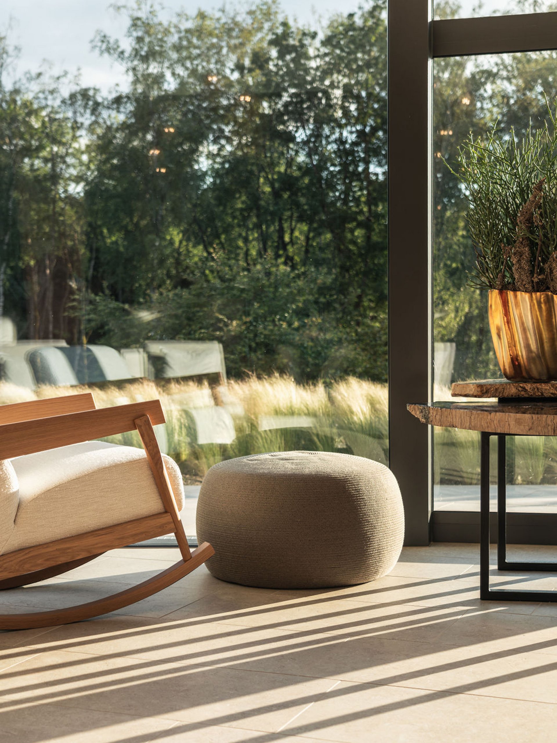 Cozy rocking chair, pouf, and table by large window overlooking green outdoor area