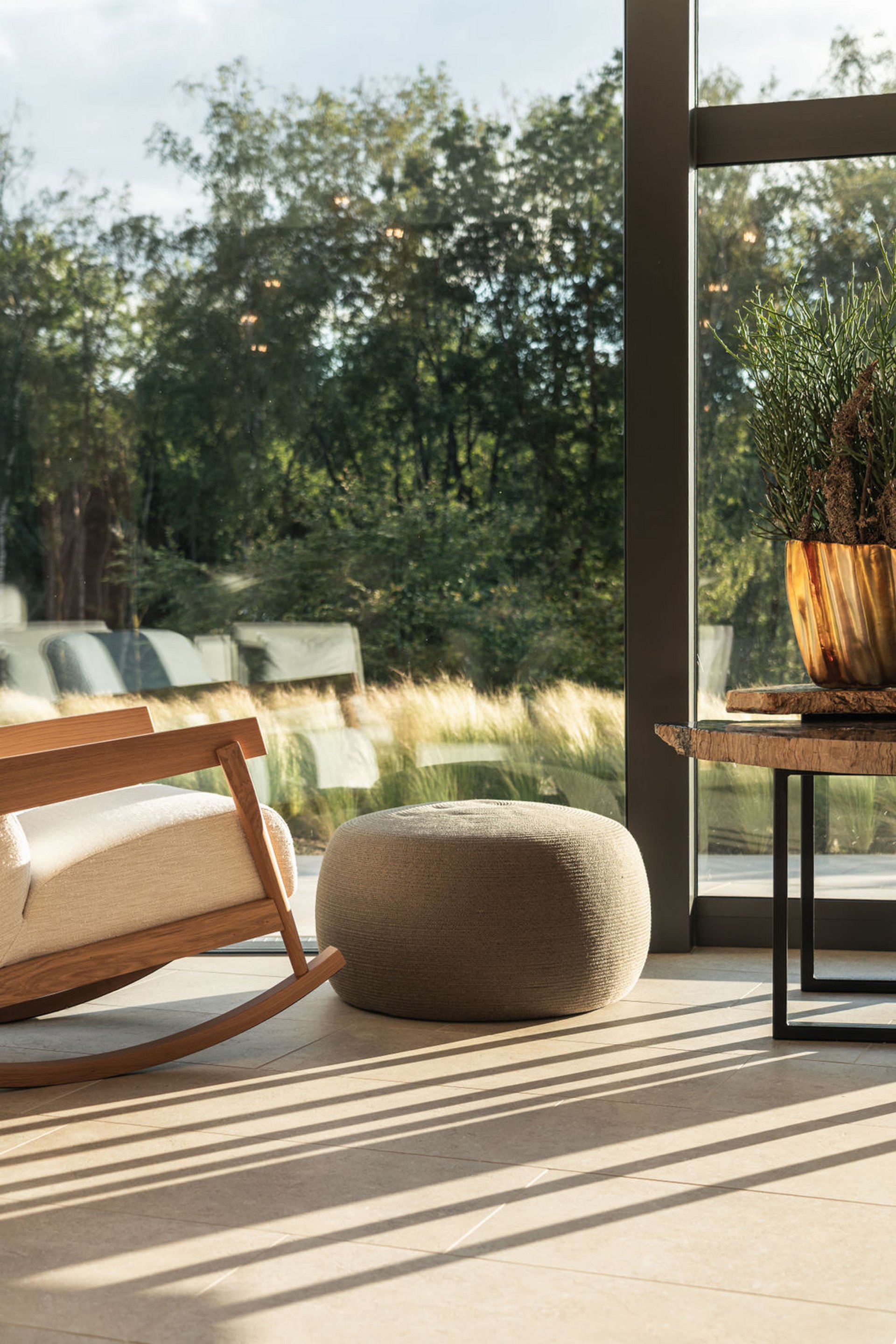 Gemütlicher Schaukelstuhl, Sitzpouf und Tisch neben großem Fenster mit Blick ins Grüne