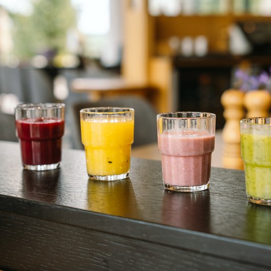 Vier verschiedene Smoothies in Gläsern auf einem Holztisch in einem Café