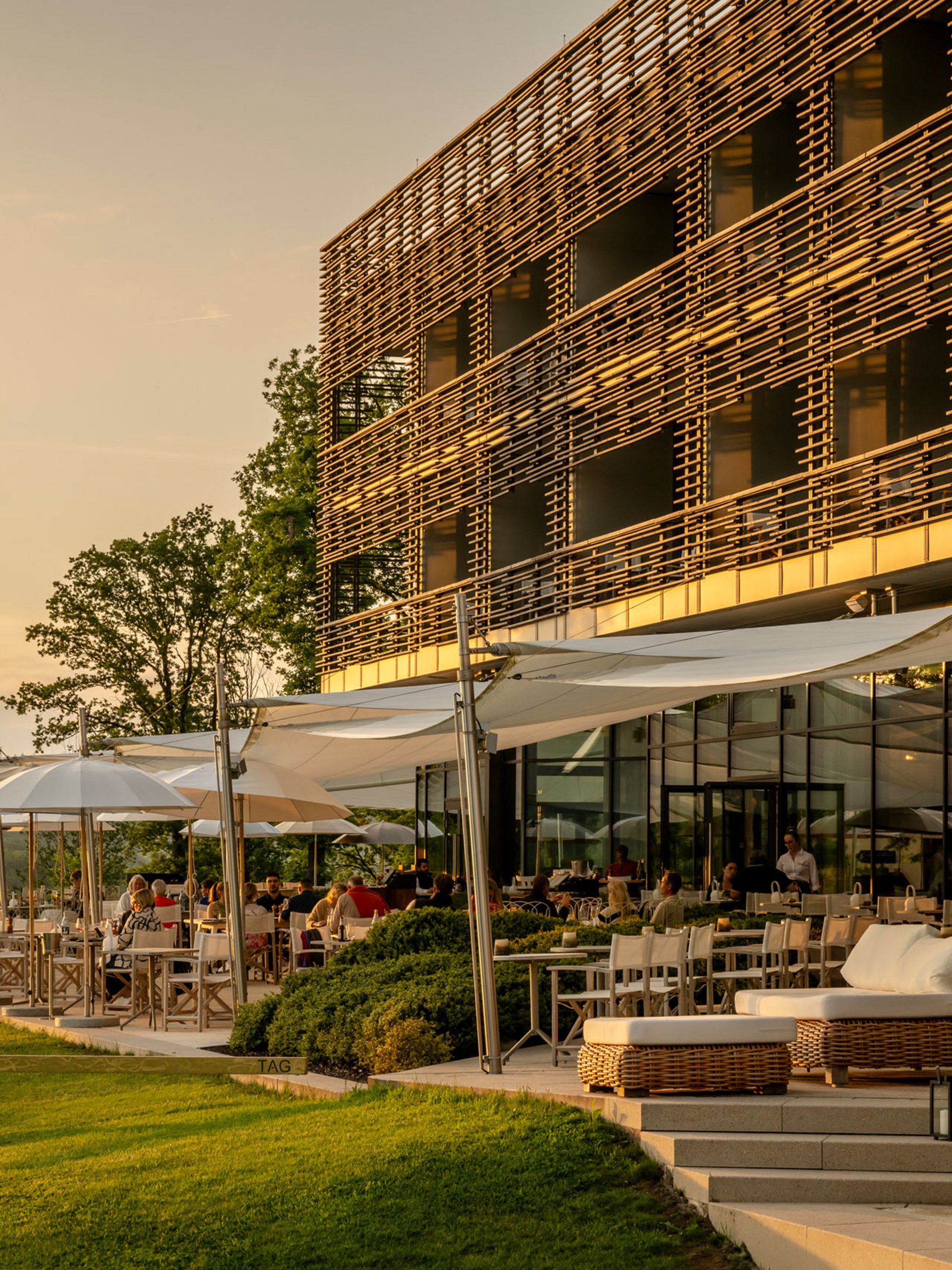 Sunny restaurant terrace with guests and modern wooden facade at sunset