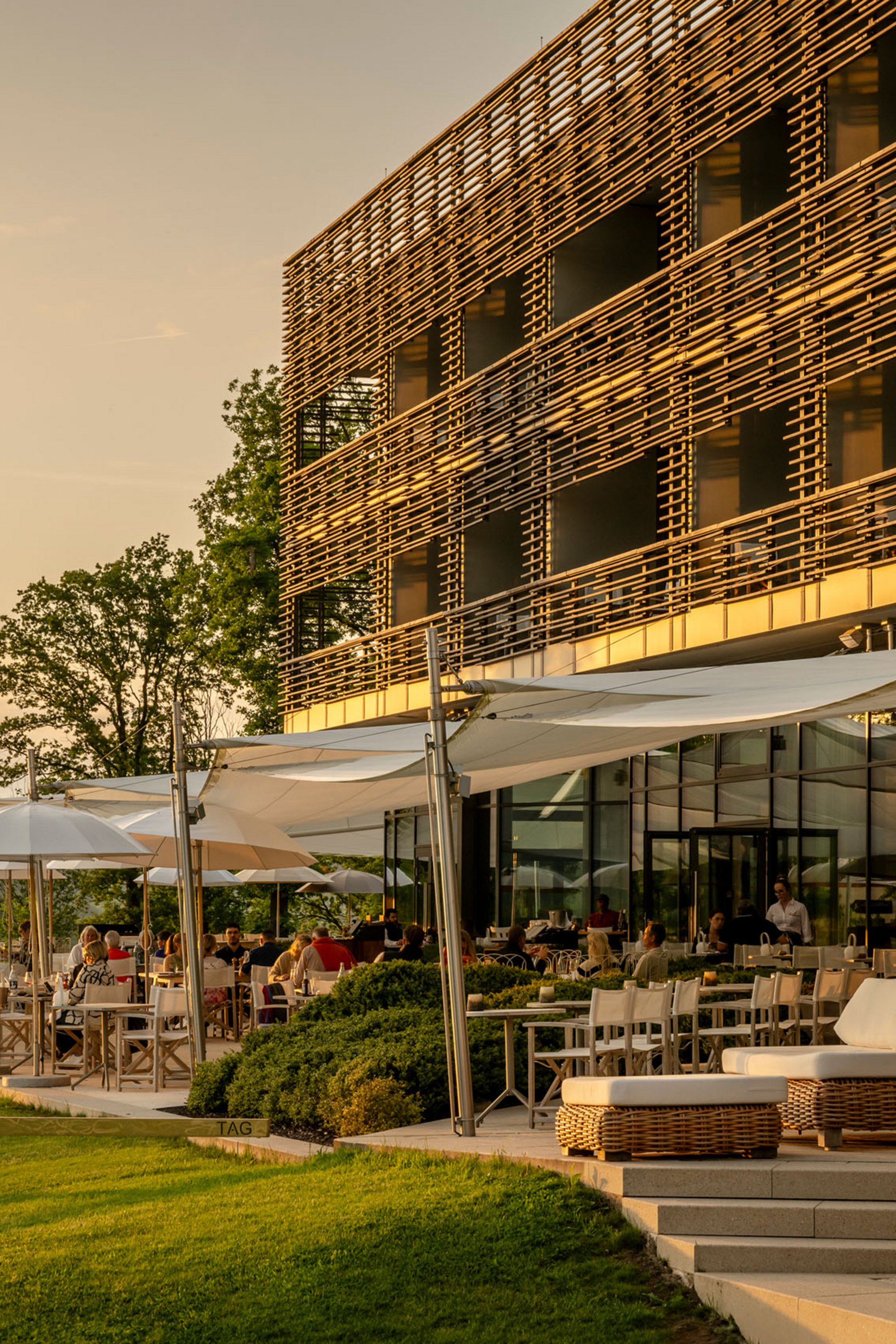 Sonnenterrasse eines Restaurants mit Gästen und moderner Holzfassade bei Sonnenuntergang