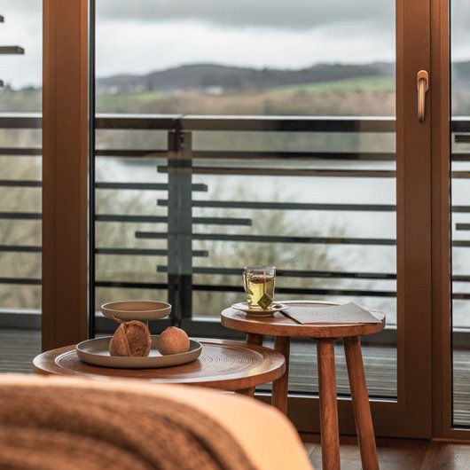 Gemütliche Holzläche mit Blick auf See hinter Glas-Schiebetür