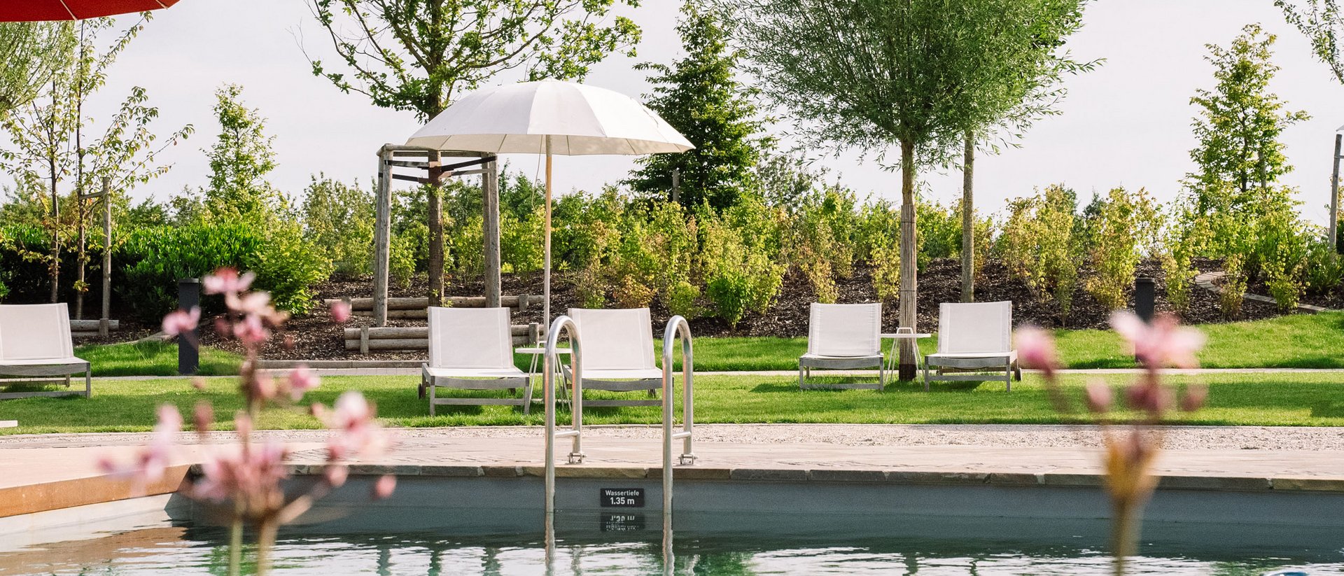 Schwimmbecken mit Liegestühlen und Sonnenschirmen in Grünanlage