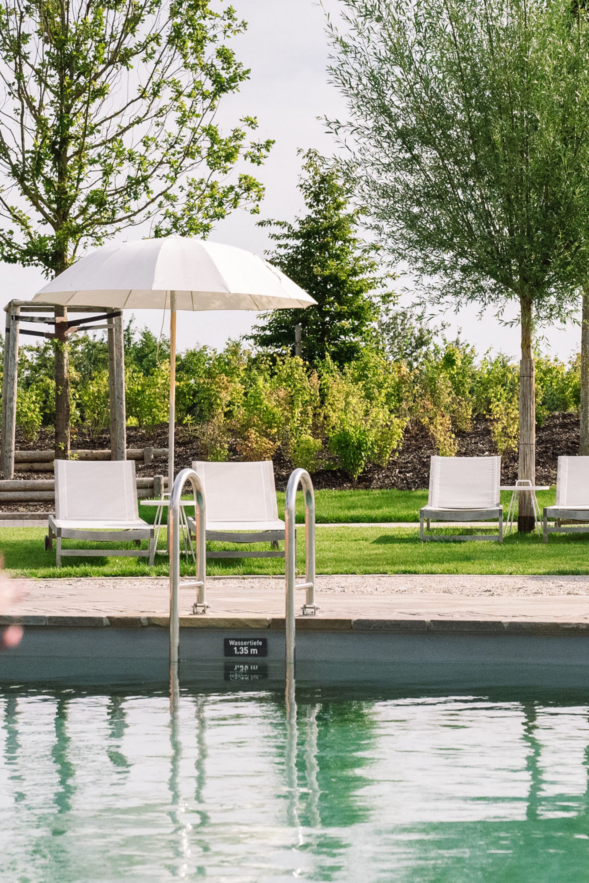 Piscine avec chaises longues et parasols dans un jardin verdoyant