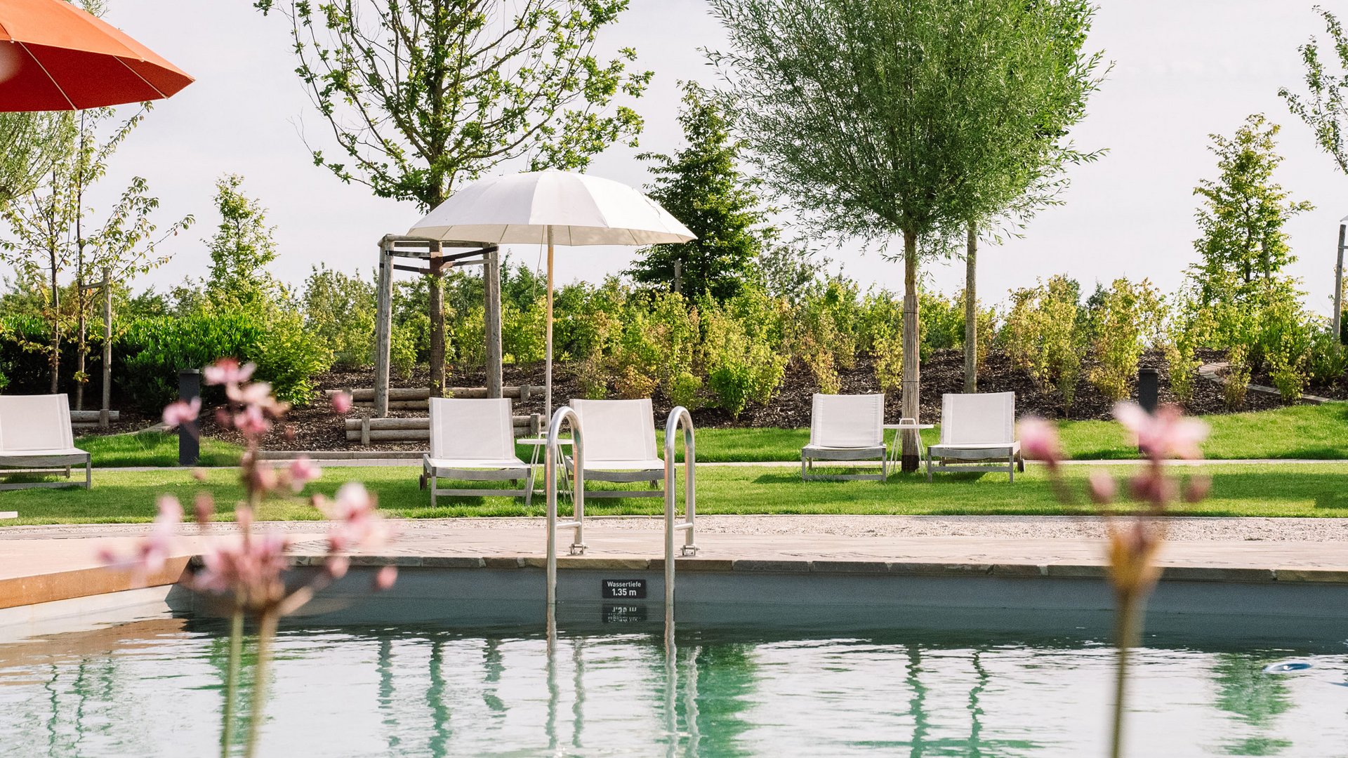 Schwimmbecken mit Liegestühlen und Sonnenschirmen in Grünanlage
