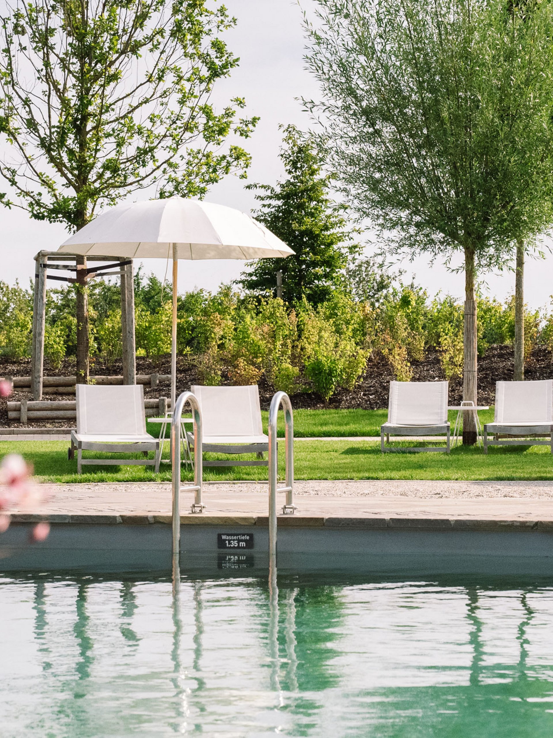 Piscine avec chaises longues et parasols dans un jardin verdoyant