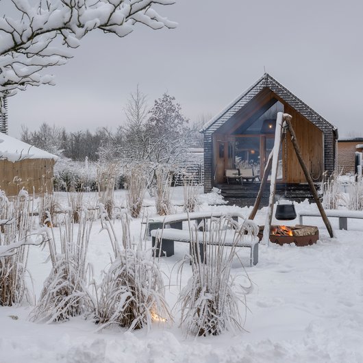 Seezeit re.connect – Bewusste Verbindung mit Natur & Kraftort Verschneite Holzhütte mit Sitzbänken und Feuerstelle im winterlichen Garten