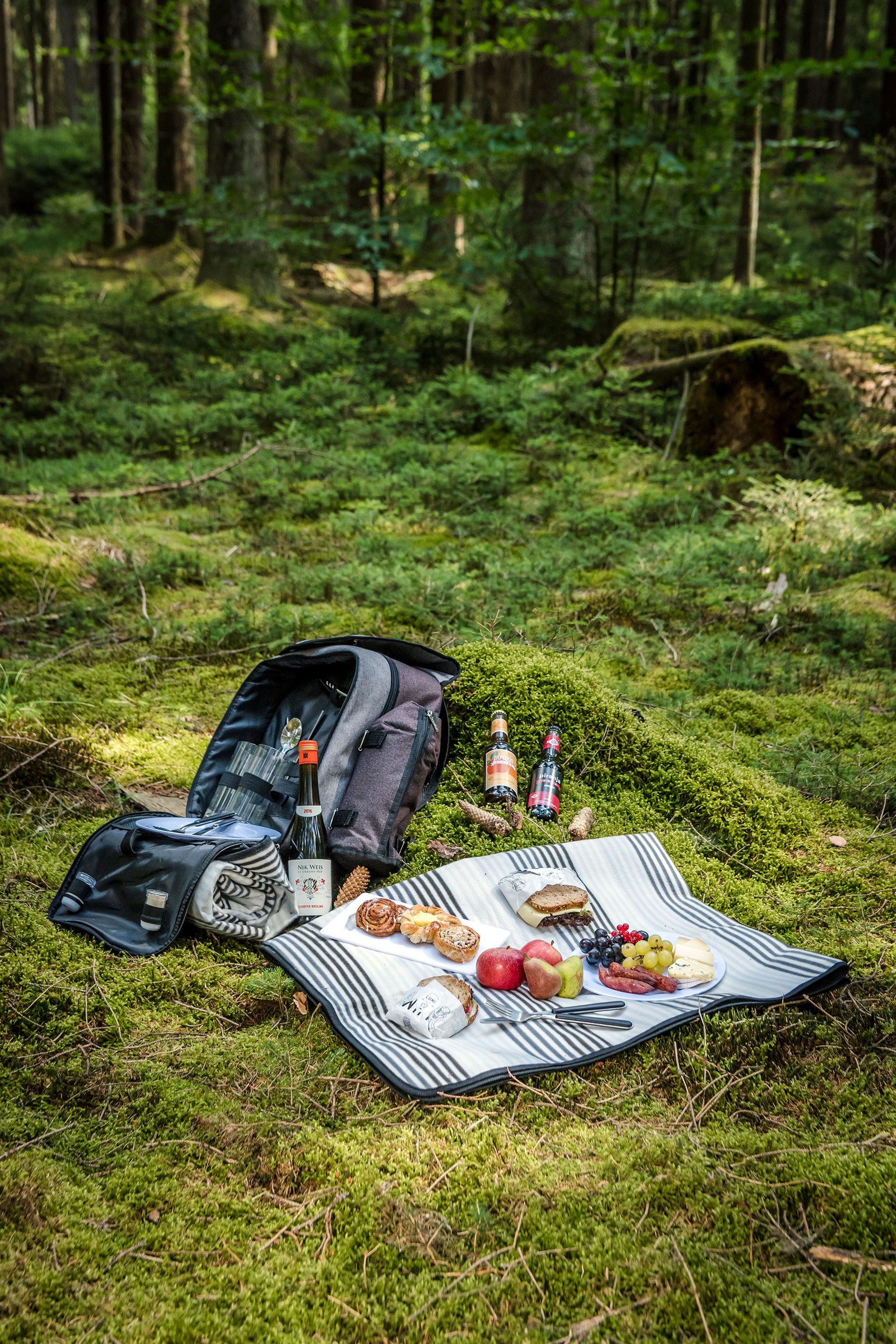 Picknick mit Essen und Getränken auf einer Decke im grünen Wald