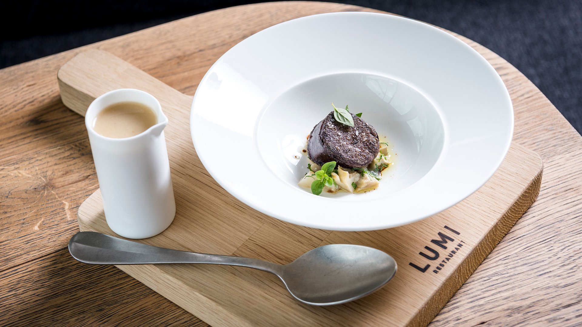Fine dining dish with sauce served on wooden board at Lumi Restaurant