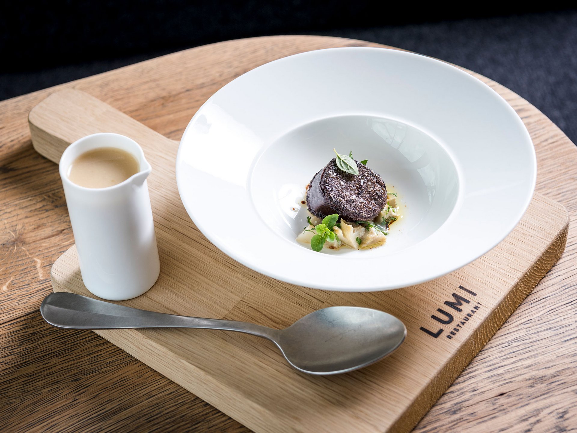 Fein angerichtete Gourmet-Speise mit Sauce, serviert auf Holzbrett im Lumi Restaurant