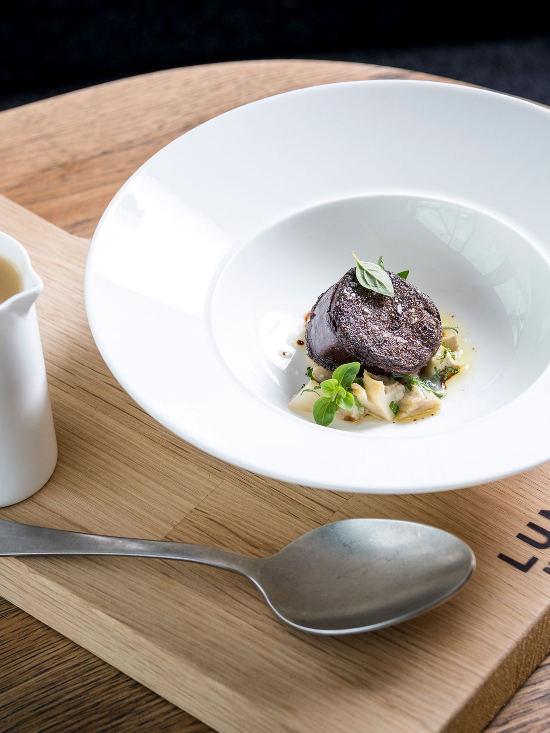Fine dining dish with sauce served on wooden board at Lumi Restaurant