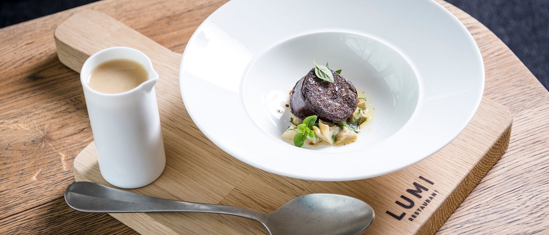 Fein angerichtete Gourmet-Speise mit Sauce, serviert auf Holzbrett im Lumi Restaurant