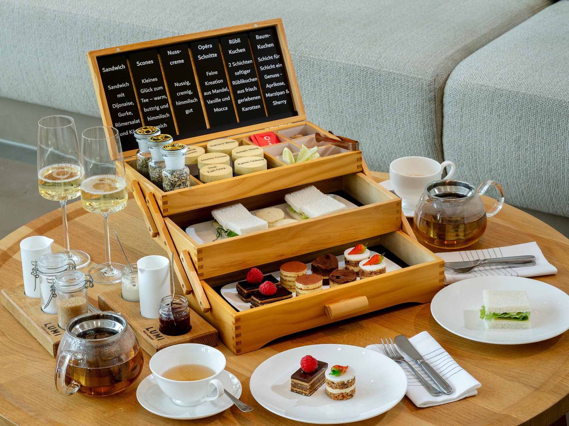 Holztablett mit Tee, Sandwiches und kleinen Kuchen auf rundem Holztisch