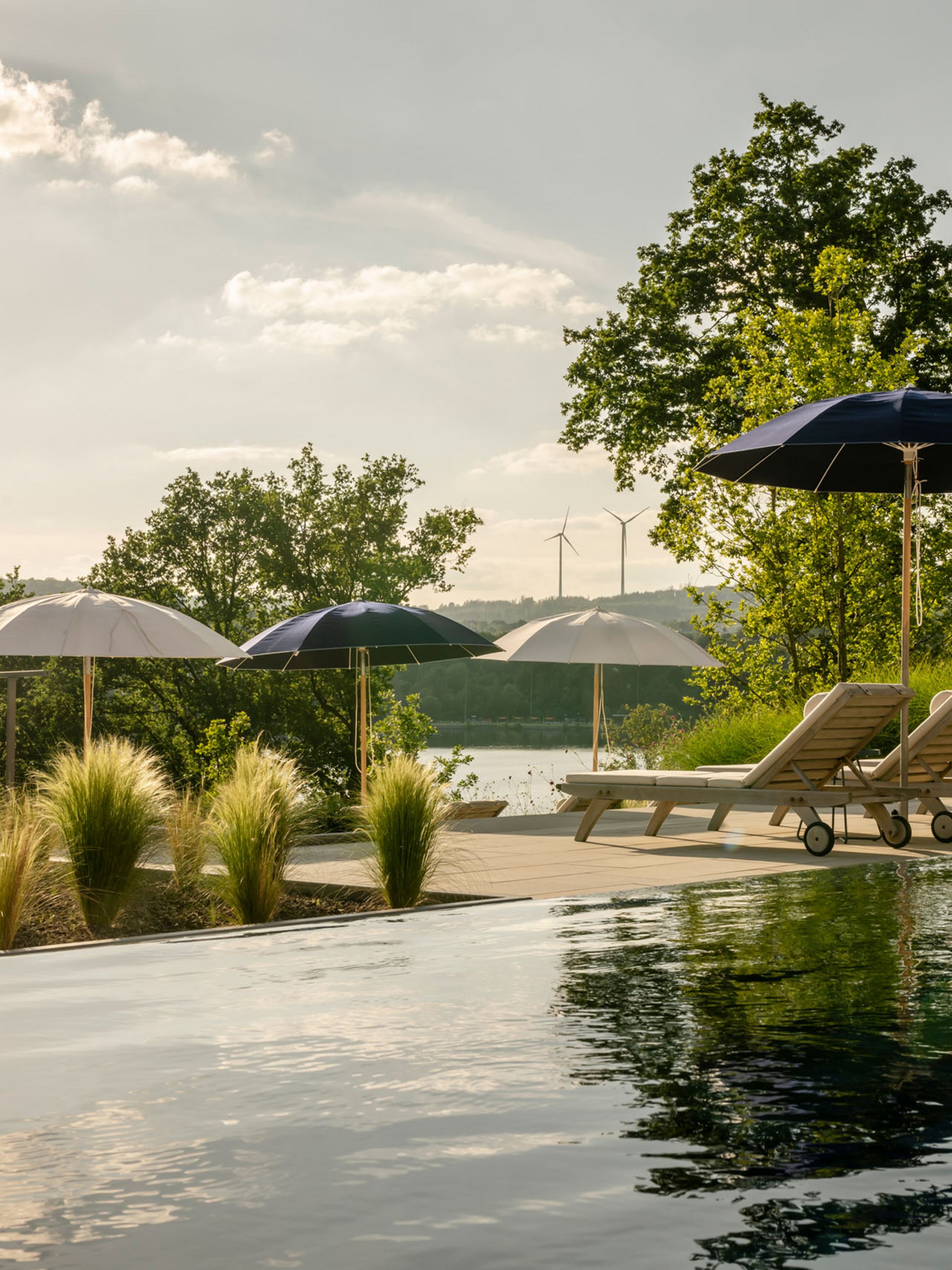 Pool with lounge chairs and umbrellas in natural landscape under sunlight