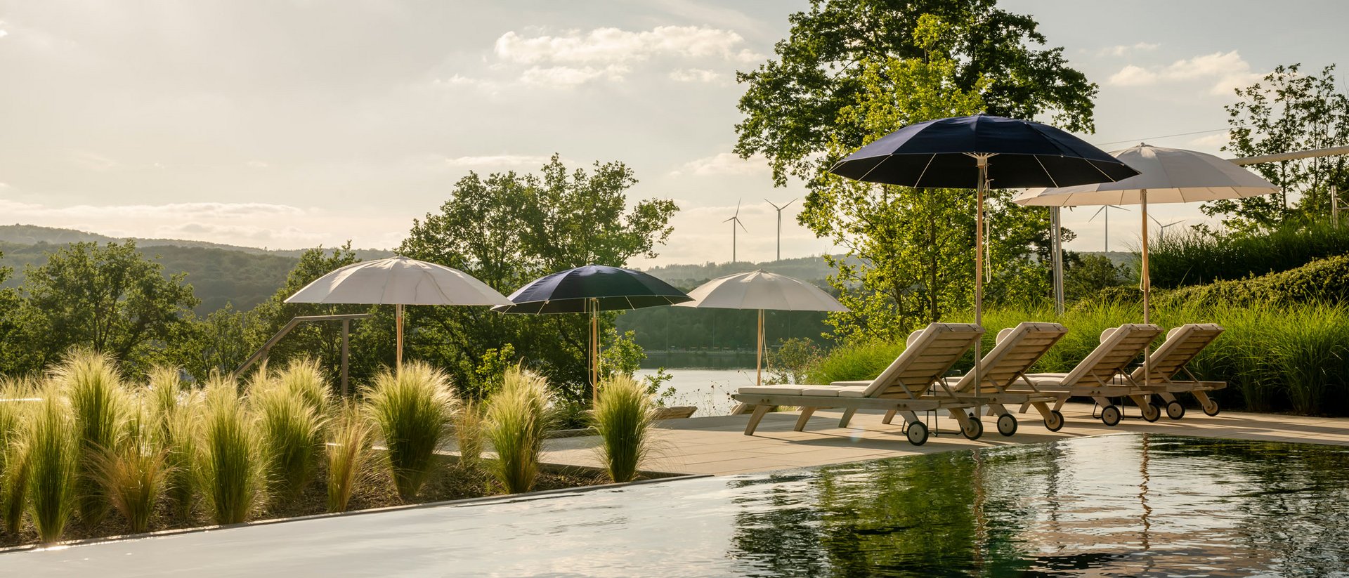 Piscine avec chaises longues et parasols dans un paysage naturel sous la lumière du soleil