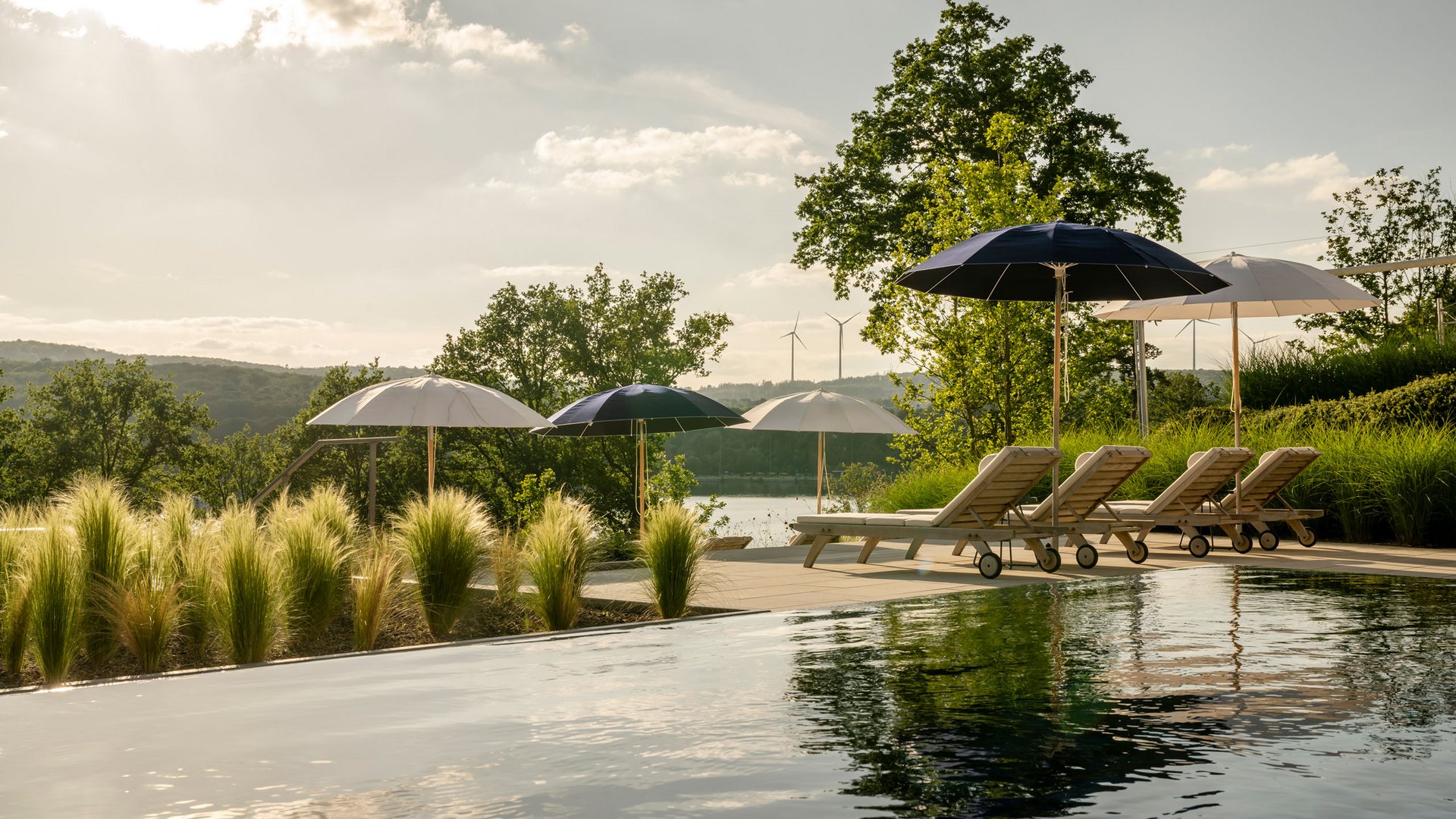 Pool with lounge chairs and umbrellas in natural landscape under sunlight