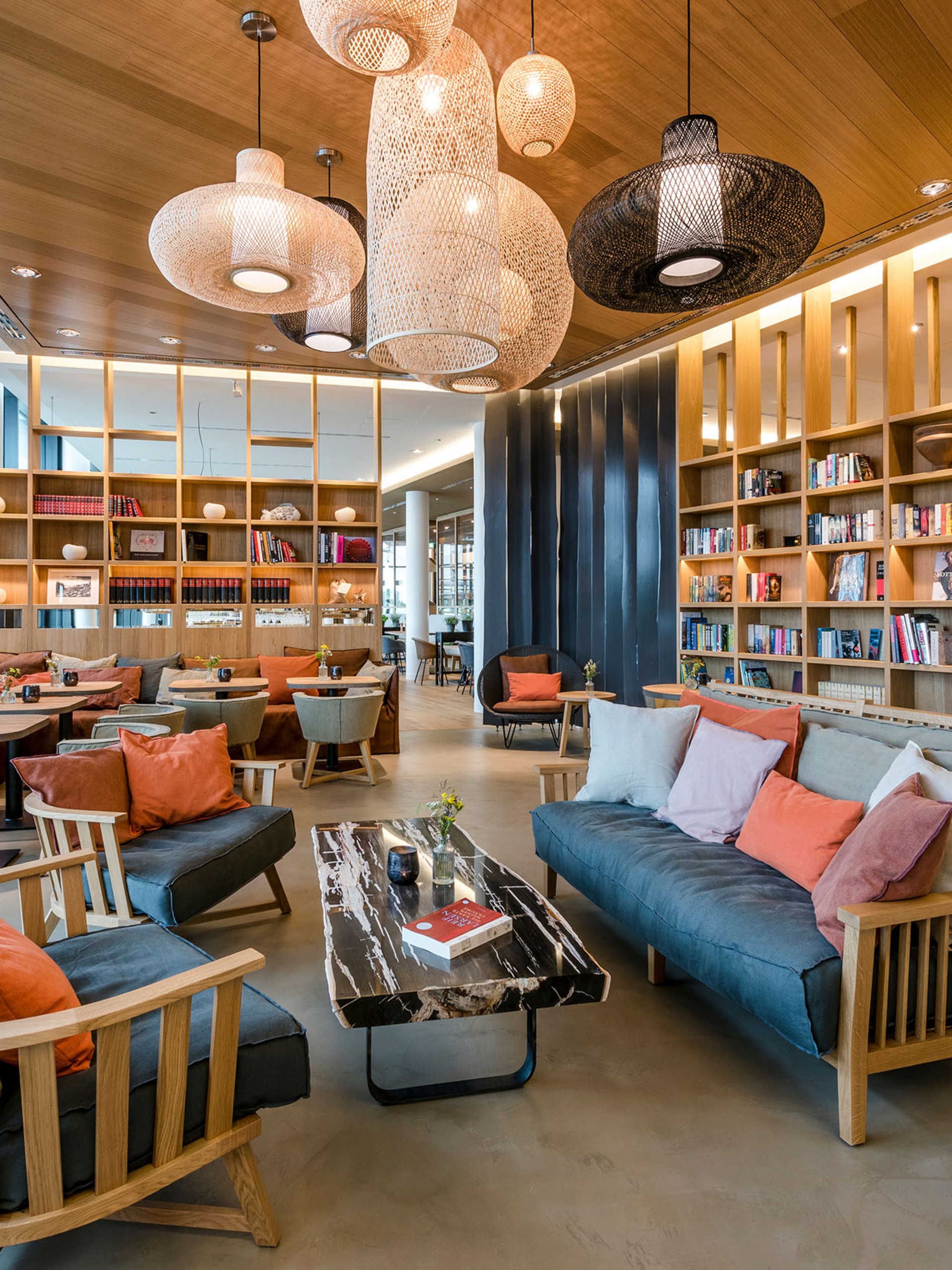 Modern library with cozy sofas, wooden shelves, and hanging lamps