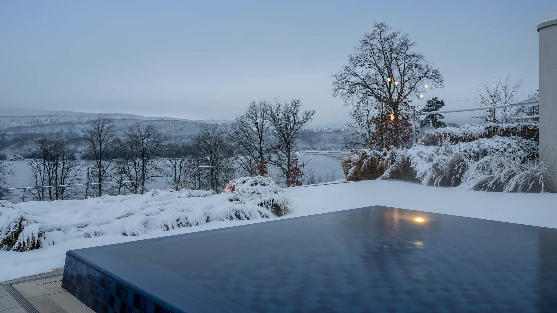 Außenpool im Schnee mit Blick auf verschneite Bäume und Hügel in der Dämmerung