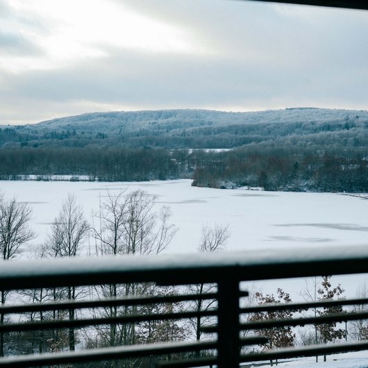 Verschneite Landschaft mit zugefrorenem See, gesehen durch ein Balkongeländer
