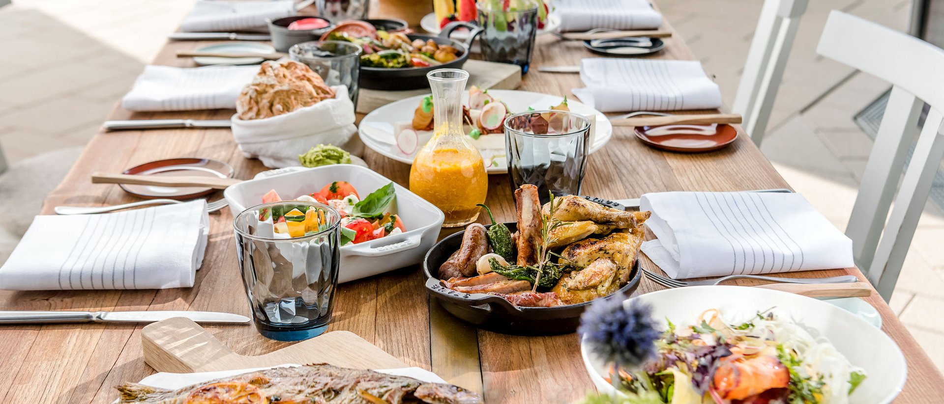 Essensauswahl auf einem Holztisch mit gebratenem Fisch, Fleisch und Salaten
