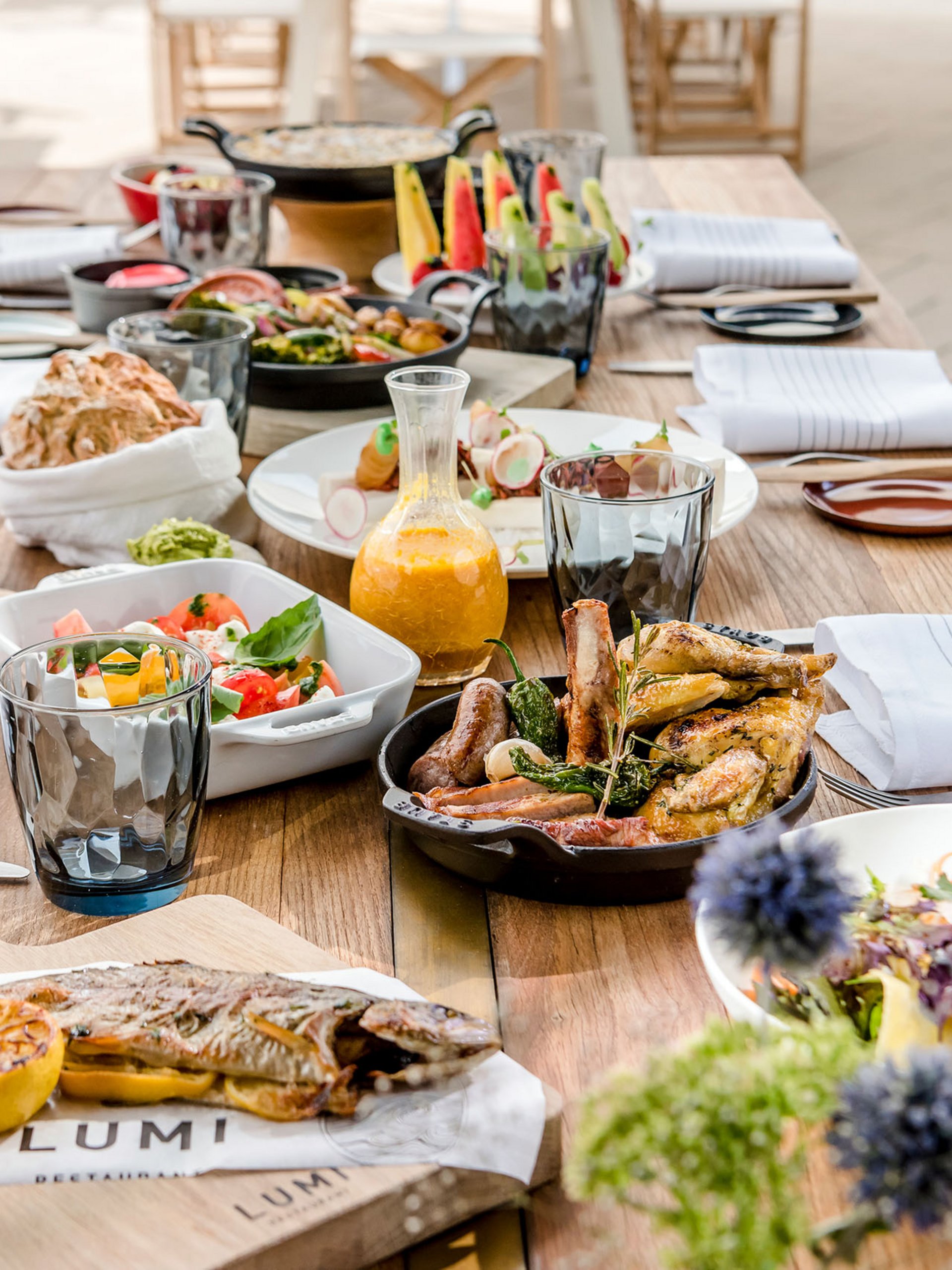 Table en bois dressée avec poisson grillé, viande et salades variées