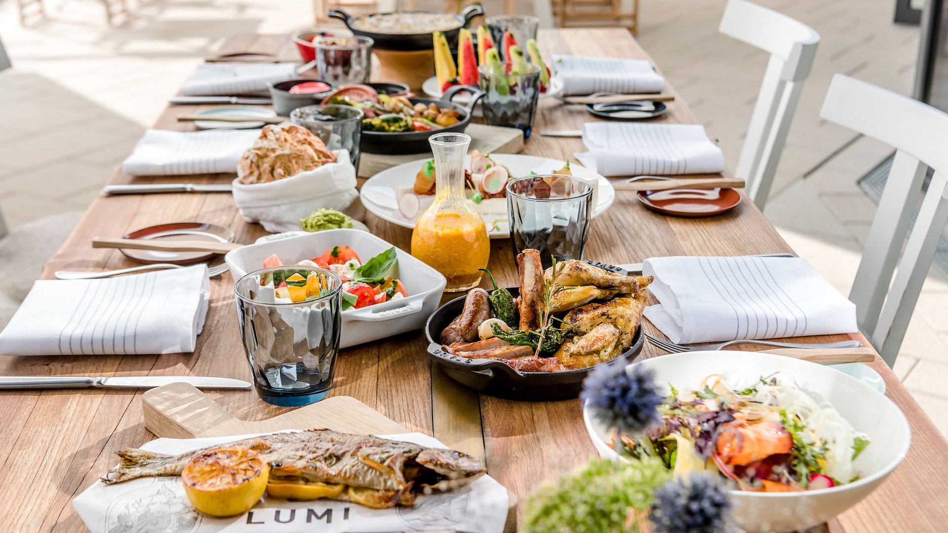 Essensauswahl auf einem Holztisch mit gebratenem Fisch, Fleisch und Salaten