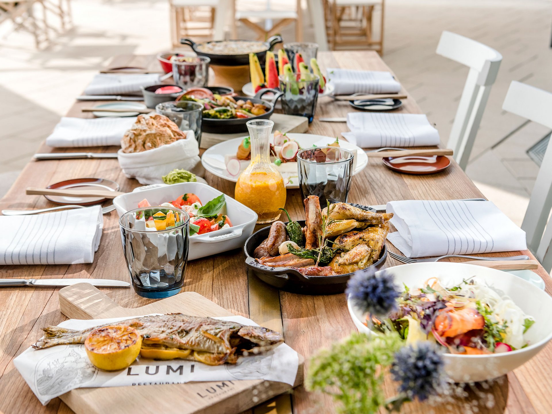 Essensauswahl auf einem Holztisch mit gebratenem Fisch, Fleisch und Salaten