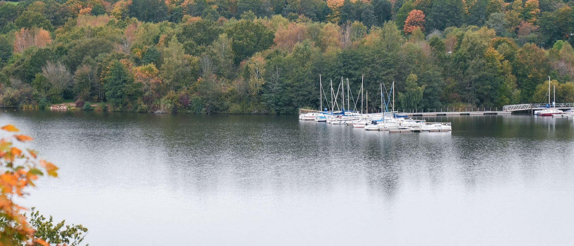 Herbstlicher See mit Yachten und bewaldeten Hügeln im Hintergrund