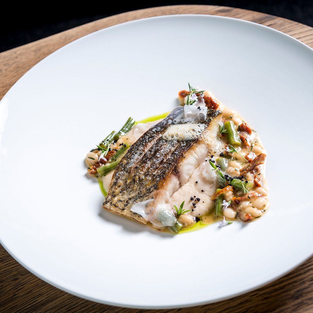 Gebratener Fischfilet mit weißen Bohnen und Gemüse auf weißem Teller